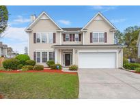 Charming two-story home with tan siding, dark shutters, a well-manicured lawn, and an attached two-car garage at 210 Sabal Palmetto Ct, Moncks Corner, SC 29461