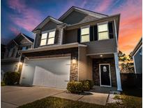 Charming two-story home with stone accents, a two-car garage, a manicured lawn, and inviting curb appeal at twilight at 449 Whispering Breeze Ln, Summerville, SC 29486
