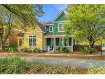 Charming yellow and green two-story home with a cozy front porch surrounded by lush landscaping at 5132 E Liberty Park Cir, North Charleston, SC 29405