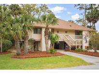 Inviting two-story condo features palm trees, well-kept lawn, and ground-level covered parking at 816 Club Cottage Rd, Edisto Beach, SC 29438