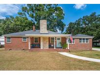 Charming brick home featuring a welcoming front porch, lush landscaping, and a classic American flag at 1756 Mchenry Ave, Charleston, SC 29412