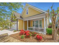 Charming yellow home with a stone garage, inviting front porch and vibrant landscaping at 2010 Redback Dr, Summerville, SC 29483