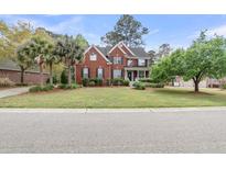 Inviting two-story red brick home with a manicured front lawn, mature trees, and a charming front porch at 1185 Out Of Bounds Dr, Summerville, SC 29485