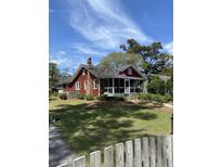 Charming red home features a screened-in porch, manicured lawn, and a classic American flag at 402 N Hickory Street St, Summerville, SC 29483