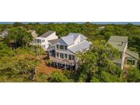 Stunning elevated home boasts a modern design, metal roof, and beautiful deck surrounded by lush greenery at 9 Marsh Island Ln, Isle of Palms, SC 29451