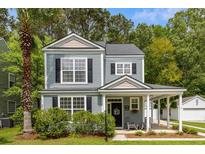 Charming two-story home with a covered front porch, manicured lawn, and a lush palm tree at 8986 N Red Maple Cir, Summerville, SC 29485