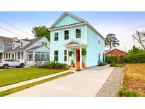 Charming two-story home with light blue siding, a red door, landscaped yard, and a concrete driveway at 1130 5Th Ave, Charleston, SC 29407