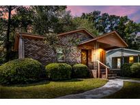 Charming brick home featuring a covered front porch, manicured bushes and a well-maintained lawn at dusk at 5447 W Lakeland Dr, North Charleston, SC 29406