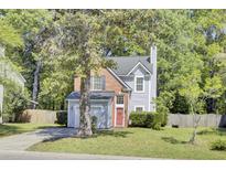 Charming two-story home with gray siding, red brick accents, mature trees, and a cozy, landscaped front yard at 1954 Treebark Dr, Charleston, SC 29414