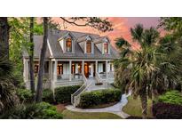 Charming two-story home with inviting front porch, landscaped yard, mature palm trees, and colorful sunset backdrop at 2104 Royal Pine Dr, Seabrook Island, SC 29455