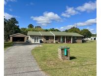 Charming single-story brick home featuring a lush lawn, and a detached two car garage, set against a backdrop of mature trees at 240 Kerrison St, Varnville, SC 29944
