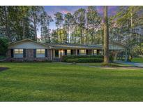 Charming brick home boasts a well-manicured lawn and mature trees at sunset at 112 Furlong Rd, Summerville, SC 29483