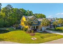 Beautiful yellow home with a lush green lawn, mature trees, and charming curb appeal on a sunny day at 1440 Teaberry Path, Charleston, SC 29414