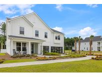 Stunning two-story home with white siding, black trim, inviting entry, beautiful landscaping and a paver sidewalk at 208 Quimby Hill Dr, Huger, SC 29450