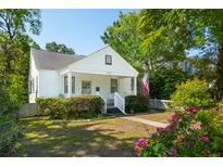 Charming white home featuring a well-manicured lawn, a quaint front porch, and the American flag at 115 Peachtree St, Charleston, SC 29403