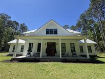 Stunning two-story farmhouse with a metal roof and a covered front porch with rocking chairs at 1183 Guerins Bridge Rd, Awendaw, SC 29429