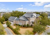A beautiful brick home showcases manicured landscaping and a three car garage on a sunny day at 185 River Green Pl, Daniel Island, SC 29492