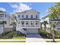 Stunning two-story beach home featuring a classic white exterior, a charming front porch, and lush tropical landscaping at 2194 Cultura Cir, Mount Pleasant, SC 29466