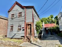 Two-story home featuring deteriorating wood siding and a small, overgrown yard needing repair at 6 Moultrie St, Charleston, SC 29403