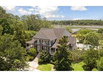 Stately home featuring a wraparound porch, mature landscaping, and a glimpse of the waterfront at 1972 Long Creek Rd, Wadmalaw Island, SC 29487