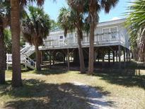 Charming coastal home elevated with a spacious deck, perfect for enjoying the surrounding palm trees and ocean breeze at 2604 Palmetto Blvd, Edisto Island, SC 29438
