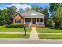 Charming brick home featuring a welcoming front porch, manicured lawn, and mature landscaping at 1069 Blockade Runner Pkwy, Summerville, SC 29485