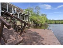 Waterfront home features a wooden dock with stairs leading up to the house, surrounded by lush greenery and a serene river view at 8487 Parkers Ferry Rd, Adams Run, SC 29426