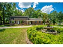 Charming brick home with well-manicured lawn, mature trees, and inviting water fountain at 100 Colonial Dr, Goose Creek, SC 29445