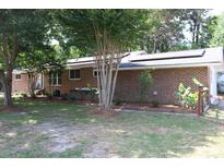 Charming brick home featuring solar panels, a well-maintained lawn, and mature trees for a serene and eco-friendly setting at 2404 Menola Ave, Charleston, SC 29414
