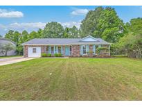 Charming brick home featuring a well-manicured lawn and inviting front porch with light blue shutters and a matching front door at 2534 Flamingo Dr, Charleston, SC 29414