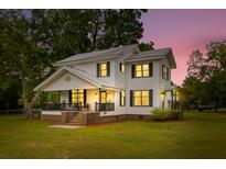 Charming two-story home with a covered porch, large yard, and warm lighting at twilight at 285 Roosevelt Dr, Saint Stephen, SC 29479