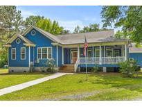 Charming blue home features a covered porch and an American flag displayed in the landscaped front yard at 6035 Bay Pond Rd, Ravenel, SC 29470