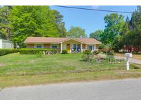 Charming single story home with bright yellow door and well-maintained front yard with flowerbeds at 1575 Langston Dr, Johns Island, SC 29455