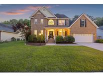 Charming brick two-story home with a well-manicured lawn and attached two-car garage at sunset at 1901 Bairds Cv, Charleston, SC 29414