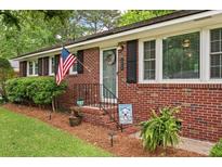 Charming brick home featuring an inviting front porch, an American flag, and a beautifully landscaped yard at 2220 Pinehurst Ave, Charleston, SC 29414