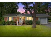 Charming brick home features a manicured lawn, a side garage, and a tree shading the front yard at 7239 Commodore Rd, Hollywood, SC 29449