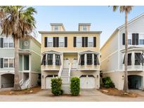 Charming yellow townhome with black shutters, white trim, stairs leading to double front doors, and a ground-level garage at 116 W 2Nd St, Folly Beach, SC 29439