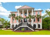 Stunning pink two-story home featuring a grand entrance, columns, and lush landscaping with palm trees at 2128 Breezy Point Dr, Mount Pleasant, SC 29466