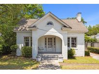Charming white brick home with arched porch, swing, and manicured landscaping at 9 Wesley Dr, Charleston, SC 29407