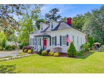 Charming white home with a red door, green shutters, dormer windows, and manicured landscaping at 318 N Magnolia St, Summerville, SC 29483