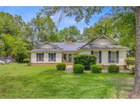 Charming ranch-style home featuring a lush green lawn, mature trees, and solar panels on the roof at 4 Garth Dr, Charleston, SC 29414