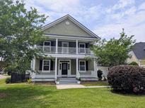 Charming two-story home features a double porch, green lawn, and mature trees enhancing curb appeal at 911 Hunt Club, Charleston, SC 29414
