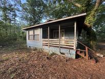 A modest, blue, single-story house with a small porch nestled in a wooded lot at 7112 Old Jacksonboro Rd, Ravenel, SC 29470