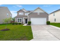 Two-story home features manicured lawn, neutral siding, stone accents, and attached two-car garage at 9711 Tackle St, Ladson, SC 29456