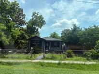 Charming single-story home with a dark color scheme surrounded by mature trees and a chain link fence at 2601 Oregon Ave, North Charleston, SC 29405
