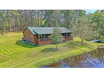 Charming log cabin home with a green metal roof, screened porch, and surrounded by a lush lawn and pond at 5519 Jefferies Hwy, Walterboro, SC 29488