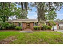 Charming brick home featuring a well-manicured lawn and lush landscaping with mature trees and Spanish moss at 614 Beauregard St, Charleston, SC 29412