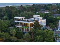 Beautiful multi-story home with multiple balconies and rooftop deck, surrounded by lush greenery at dusk at 2213 Rolling Dune Rd, Seabrook Island, SC 29455