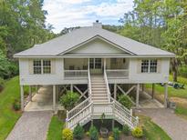 Charming two-story stilt home with a front porch, and manicured front yard and mature trees at 8346 Chisolm Plantation Rd, Edisto Island, SC 29438