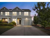 Charming two-story home with gray siding, attached garage, well-manicured lawn and blooming bushes in front at 132 Wild Holly Dr, Moncks Corner, SC 29461